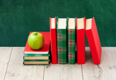 Okula geri döndüm, renkli kapaklar içinde bir yığın kitap ve boş yeşil okul yönetim kurulu geçmişli ahşap masa üzerinde yeşil elma. Uzaktan eğitim. Karantina konsepti: