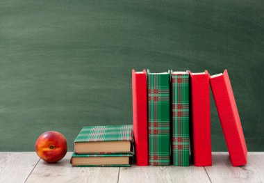 Okula geri döndüm, renkli örtüler içinde bir yığın kitap ve boş yeşil okul yönetim kurulu geçmişli ahşap masada kırmızı şeftali. Uzaktan eğitim. Karantina konsepti: