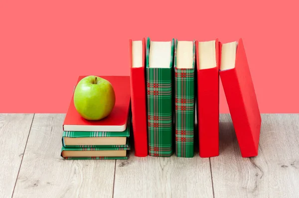 Back to school, pile of books in colorful covers and green apple on wooden table with red pink background. Distance home education. Quarantine concept of stay home