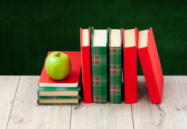 Okula geri döndüm, renkli kapaklar içinde bir yığın kitap ve boş yeşil okul yönetim kurulu geçmişli ahşap masa üzerinde yeşil elma. Uzaktan eğitim. Karantina konsepti: