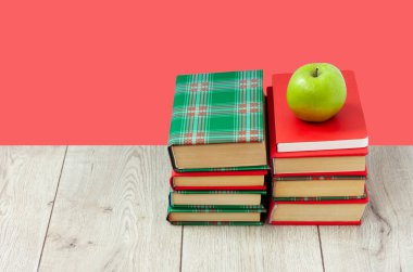 Okula geri döndüm, renkli örtüler içinde bir yığın kitap ve kırmızı pembe arka planlı ahşap masada yeşil elma. Uzaktan eğitim. Karantina konsepti: