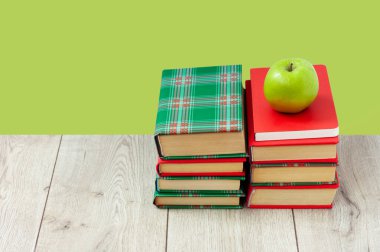 Okula geri döndüm, renkli örtüler içinde bir yığın kitap ve yeşil nane yeşili arkaplanlı ahşap masa üzerinde yeşil elma. Uzaktan eğitim. Karantina konsepti:
