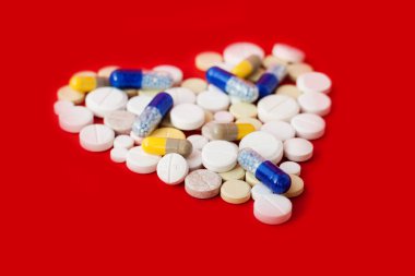 Kalp şeklinde renkli haplar, tabletler ve kapsüller beyaz arka planda. Tedavi için ilaç reçetesi sağlık hizmetleri konsepti, fotokopi alanı ile üst görünüm