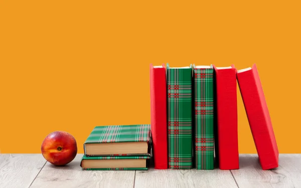 Back to school, pile of books in colorful covers and red peach on wooden table with empty orange background. Distance home education. Quarantine concept of stay home