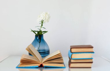 Konforlu ev dekorasyonu: cam bir masanın üzerinde beyaz çiçekli vazo ve kitap yığını. Uzak ev eğitimi. Evde kalma karantina kavramı.