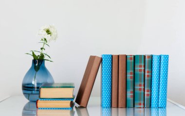 Konforlu ev dekorasyonu: cam bir masanın üzerinde beyaz çiçekli vazo ve kitap yığını. Uzak ev eğitimi. Evde kalma karantina kavramı.