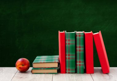 Okula geri döndüm, renkli örtüler içinde bir yığın kitap ve boş yeşil okul yönetim kurulu geçmişli ahşap masada kırmızı şeftali. Uzaktan eğitim. Karantina konsepti:
