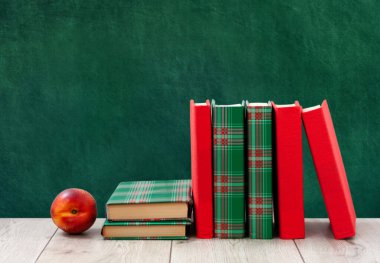 Okula geri döndüm, renkli örtüler içinde bir yığın kitap ve boş yeşil okul yönetim kurulu geçmişli ahşap masada kırmızı şeftali. Uzaktan eğitim. Karantina konsepti: