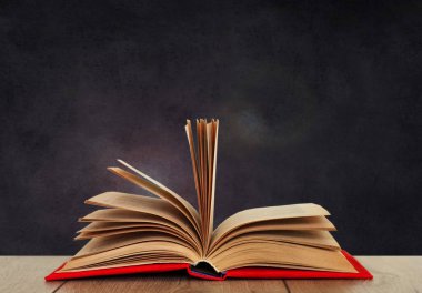 Siyah bir okulun kara tahtasının arkasındaki tahta bir masanın üzerinde kırmızı bir kapakta açık kitap kitabı. Okul mesafesindeki ev eğitimine geri dönüyoruz. Evde kalma karantina kavramı.