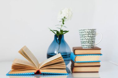 Konforlu ev dekorasyonu: bir yığın kitap, bir fincan kahve ve cam bir masanın üzerinde beyaz çiçekli vazo. Uzak ev eğitimi. Evde kalma karantina kavramı.