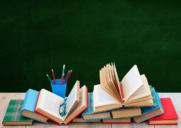 Back to school, pile of books in colorful covers and on wooden table with empty green school board background. Distance home education.Quarantine concept of stay home