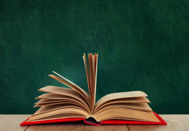 Ahşap bir masanın üzerinde, yeşil bir okulun kara tahtasının üzerinde kırmızı bir kapakta açık bir kitap kitabı. Okul mesafesindeki ev eğitimine geri dönüyoruz. Evde kalma karantina kavramı.