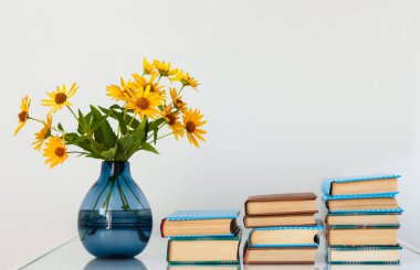 Konforlu ev dekorasyonu: Masasında sarı çiçekler olan bir yığın kitap ve vazo. Uzak ev eğitimi. Evde kalma karantina kavramı.