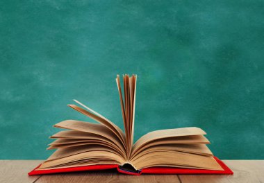 Ahşap bir masanın üzerinde, yeşil bir okulun kara tahtasının üzerinde kırmızı bir kapakta açık bir kitap kitabı. Okul mesafesindeki ev eğitimine geri dönüyoruz. Evde kalma karantina kavramı.