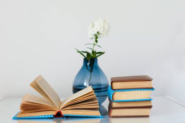 Konforlu ev dekorasyonu: cam bir masanın üzerinde beyaz çiçekli vazo ve kitap yığını. Uzak ev eğitimi. Evde kalma karantina kavramı.