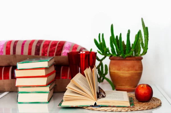舒适的室内装饰 一杯咖啡 一堆书 盆中的植物 打开的书和柳条架上的红桃 白色桌子上的枕头 远距离家庭教育 待在家里 的检疫概念 免版税图库照片