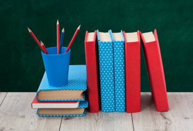 Renkli kapaklarda kitap yığını ve ahşap masa üzerinde yeşil karatahta arka planı olan kalemler. Uzaktan eğitim. Okula dönmek, karantina konsepti evde kalmak.