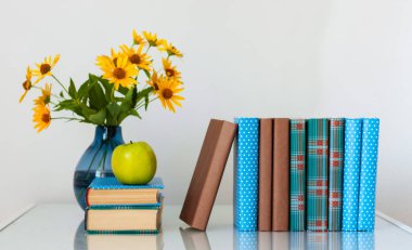 Konforlu ev dekorasyonu: Masasında sarı çiçekler olan bir yığın kitap ve vazo. Uzak ev eğitimi. Evde kalma karantina kavramı.