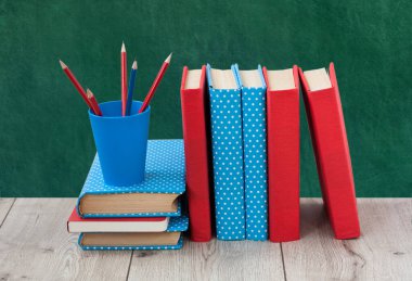 Renkli kapaklarda kitap yığını ve ahşap masa üzerinde yeşil karatahta arka planı olan kalemler. Uzaktan eğitim. Okula dönmek, karantina konsepti evde kalmak.