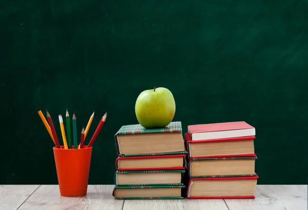 カラフルな表紙の本の山 緑の黒板の背景と木製のテーブルの上にホルダーと緑のリンゴで鉛筆 遠隔家庭教育 学校に戻ると 家に留まるという隔離概念 — ストック写真