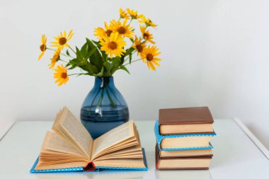 Konforlu ev dekorasyonu: Masasında sarı çiçekler olan bir yığın kitap ve vazo. Uzak ev eğitimi. Evde kalma karantina kavramı.