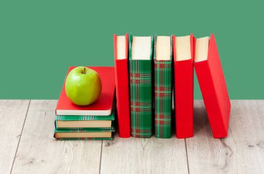 Okula geri döndüm, renkli örtüler içinde bir yığın kitap ve yeşil arka planlı ahşap masa üzerinde yeşil elma. Uzaktan eğitim. Karantina konsepti: