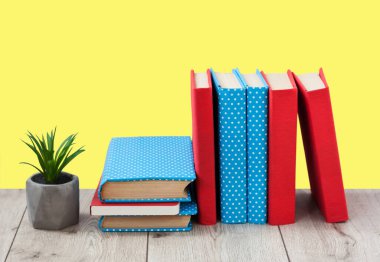 Renkli kapaklarda kitap yığını ve sarı arka plandaki ahşap masada saksıya bitki. Okul mesafesindeki ev eğitimine geri dönüyoruz. Evde kalma karantina kavramı.