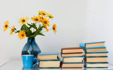 Konforlu ev dekorasyonu: Masasında sarı çiçekler olan bir yığın kitap ve vazo. Uzak ev eğitimi. Evde kalma karantina kavramı.