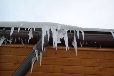 Çatıdaki buz saçakları siyah bir arka planda. Çatıdan sarkan buz saçakları.