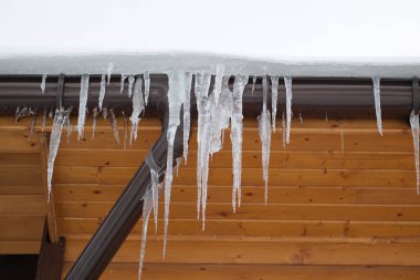 Çatıdaki buz saçakları siyah bir arka planda. Çatıdan sarkan buz saçakları.