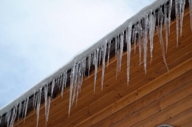 Çatıdaki buz saçakları siyah bir arka planda. Çatıdan sarkan buz saçakları.