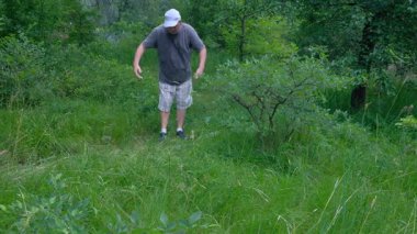 Ormanda orta yaşlı bir adam kareli şortlu ve beyaz şapkalı turistle yürürken yavaşça hava soluyor. Yüksek kalite 4k görüntü