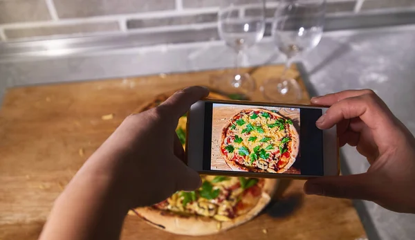 The process of photographing a cooked pizza on a smartphone
