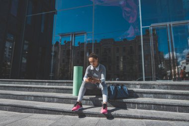 Modern bir binanın merdivenlerinde oturan genç bir kadın.