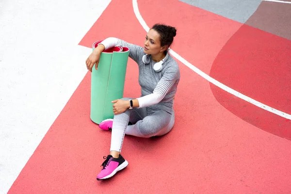 Genç kadın çocuk parkında oturuyor, paspası tutuyor ve yan tarafa bakıyor.