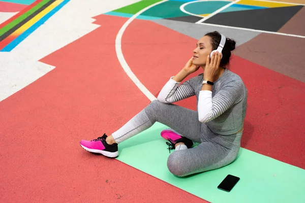 Young Woman Gray Tracksuit Sits Green Mat Wearing Headphones — Stock Photo, Image