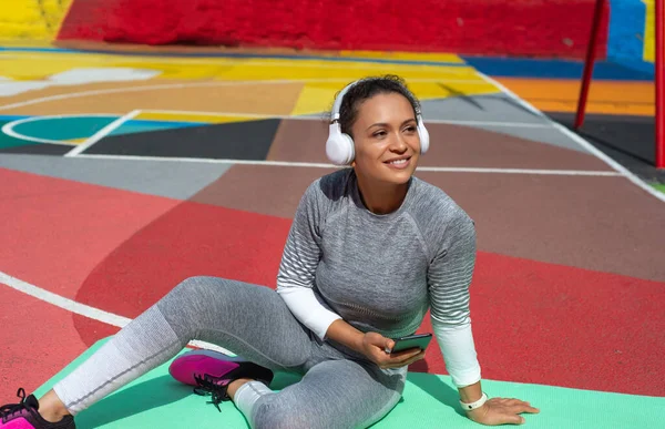 Young Woman Gray Tracksuit Sits Green Mat Headphones Smartphone Hand — Stock Photo, Image