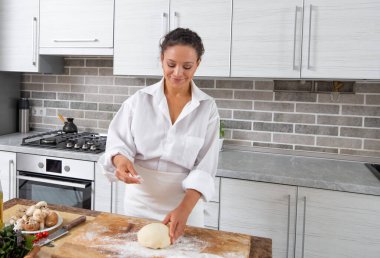 Genç kadın mutfakta yemek pişiriyor tahtanın üzerindeki hamura un serpiyor..