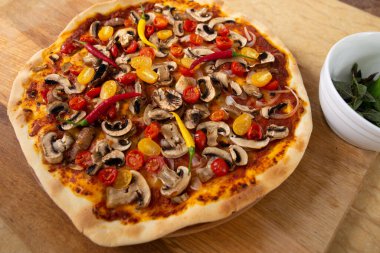 Fırından yeni çıkmış pizzanın üst görüntüsü. Sırada bitkilerle dolu bir tabak var. Vejetaryen yemeği.