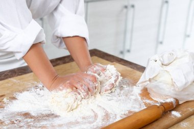 Yakın plan. Bir aşçı hamuru elleri tahtanın üzerinde yoğurur..