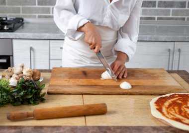 Yakından bakınca, şef soğanı tahta bir tahtanın üzerinde bıçakla kesiyor. Ön görünüm.