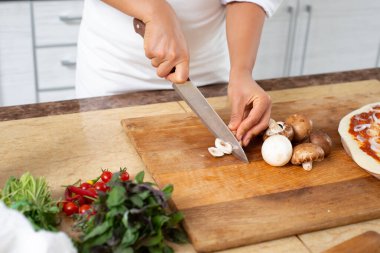 Ahşap bir tahtanın üzerinde mantar kesen şefin elleri. Ön görünüm.