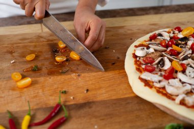Ahşap bir tahtanın üzerinde sarı kiraz domatesli bıçakla doğrayan bir şefin elleri görülüyor. Vejetaryen pizzası yapıyorum..