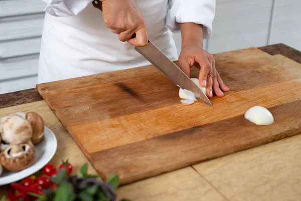 Close-up, chef cuts the onion with a knife on a wooden board.