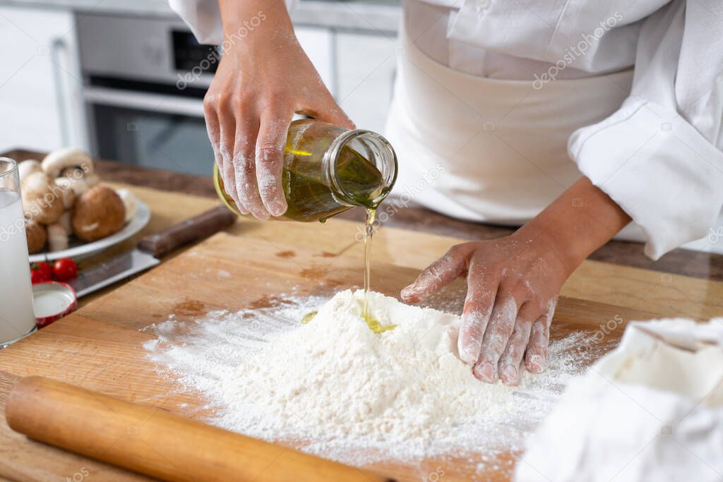 Close-up. A cook pours olive oil from a bottle into a handful of flour on the table.