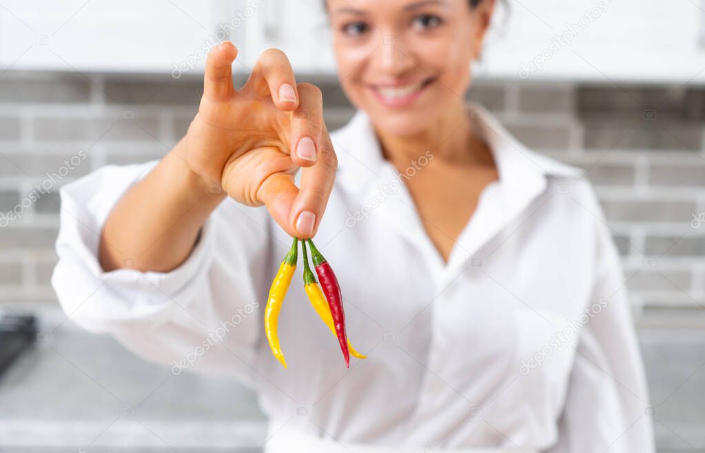 Close-up the young woman chef holding hot peppers with fingers. The woman smiles.