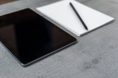 Tablet görünümlü gri bir masaüstü parçası ve kurşun kalemli bir defter görünümü.