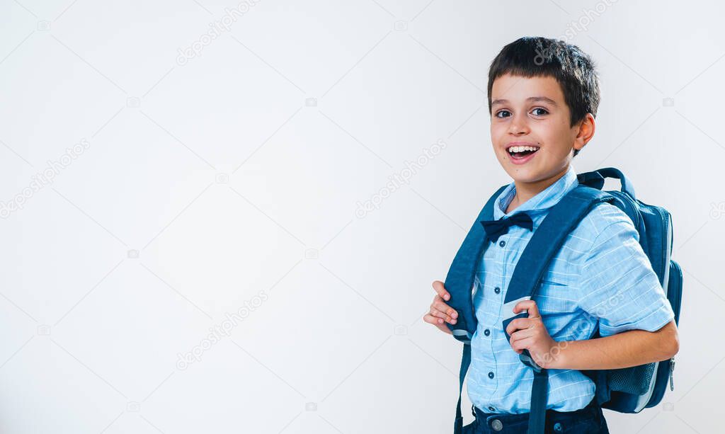 The schoolboy in a shirt with a bow tie and a backpack behind his back stands half a turn and laughs. Conceptual. Copy space.