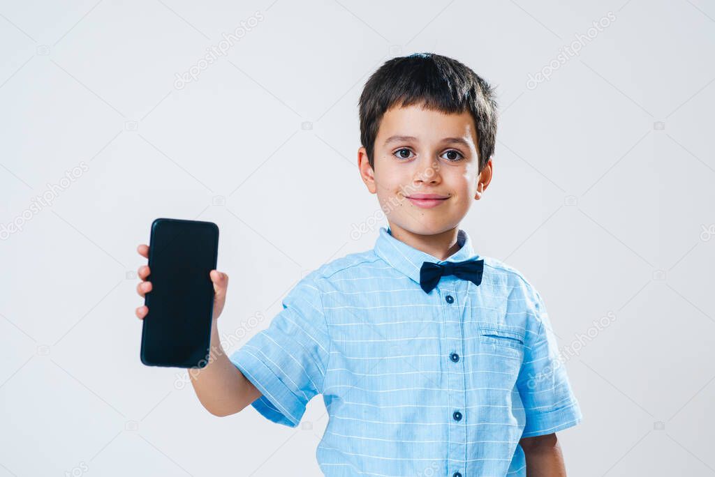 The schoolboy in a shirt with a bow tie demonstrates a smartphone screen. Conceptual. Copy space.