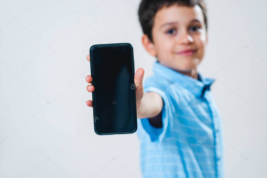 The schoolboy in a shirt with a bow tie demonstrates a smartphone screen. Focus on the smartphone. Conceptual. Copy space.
